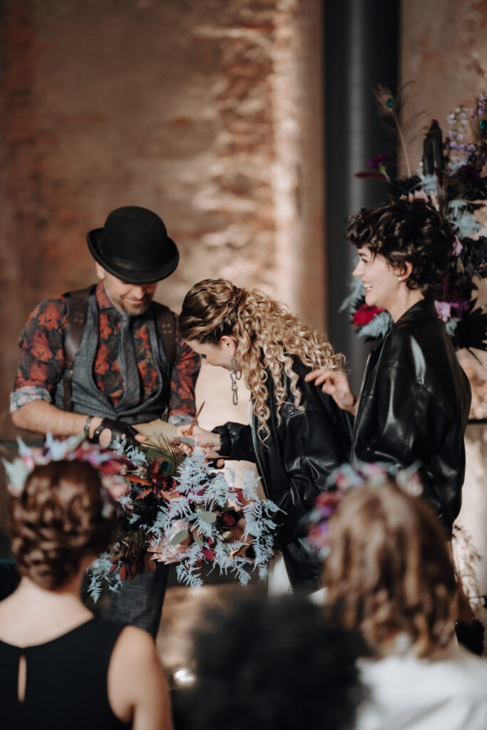 Drei Personen in stilvollen Outfits stehen bei einem eleganten Hochzeitsevent in Österreich neben Blumenarrangements zusammen.