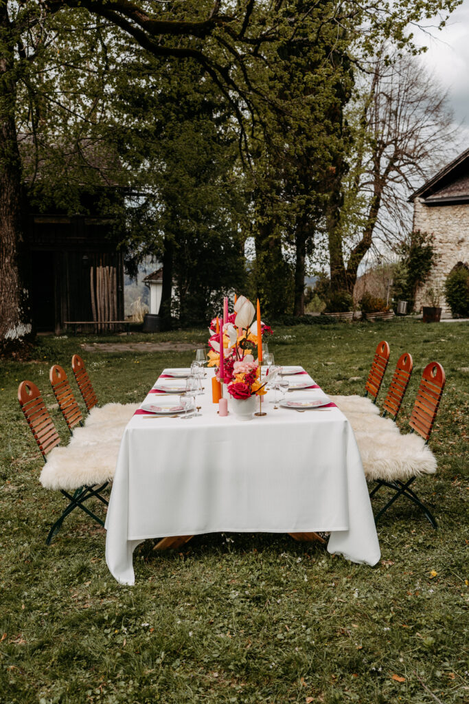 Ein für ein Essen gedeckter Tisch im Freien mit bunten Blumen, Kerzen und Holzstühlen auf einer Wiese - perfekt für eine Hochzeit in Österreich, kuratiert von einer erfahrenen Hochzeitsplanerin.