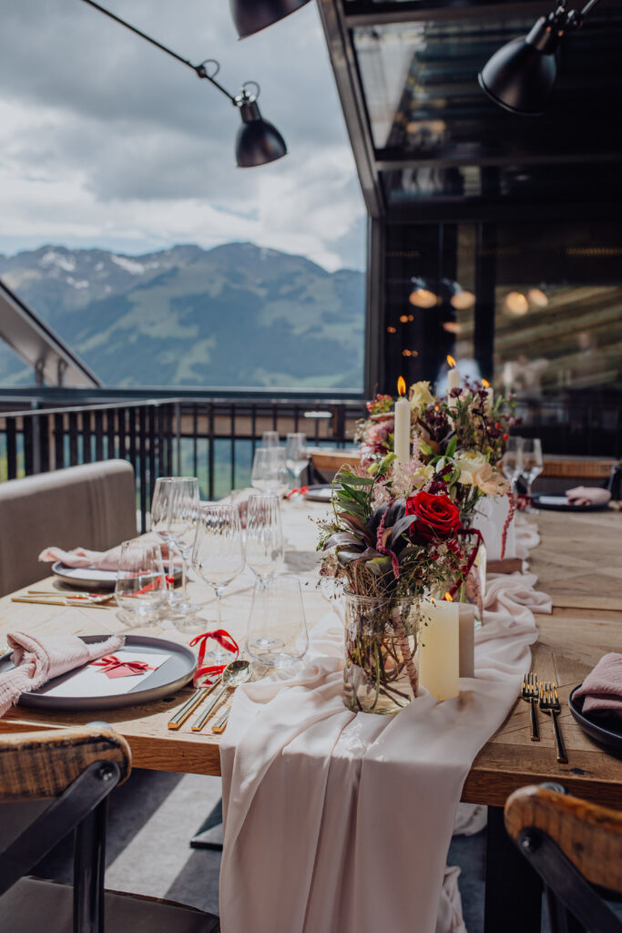 Eleganter Esstisch im Freien mit Blumen, Kerzen und Gläsern inmitten einer Berglandschaft - perfekt für eine romantische Hochzeitslocation in Österreich.