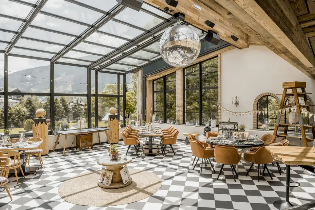 Sonniger, gläserner Speisesaal mit kariertem Boden, braunen Stühlen und einer großen, von der Decke hängenden Discokugel - eine ideale Hochzeitslocation in Österreich für Paare, die von einer einzigartigen und lebhaften Atmosphäre träumen. Heiraten im Sendlhofers im Salzburger Land