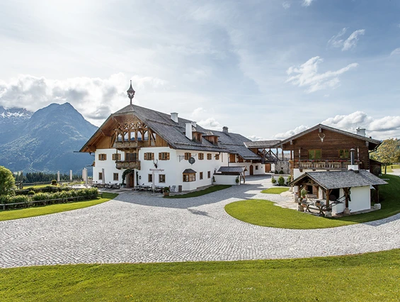 Großes alpenländisches Haus mit hölzernen Akzenten, Bergkulisse, blauem Himmel und gepflegtem Rasen - eine ideale Hochzeitslocation in Österreich für alle, die von Heiraten in Österreich träumen.