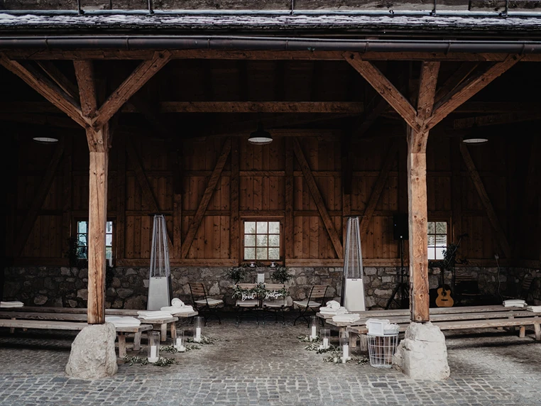 Rustikaler Holzpavillon mit Bänken, Heizstrahlern, Dekoration und einer Gitarre auf Steinboden - eine bezaubernde Hochzeitslocation in Österreich für Ihren besonderen Tag.