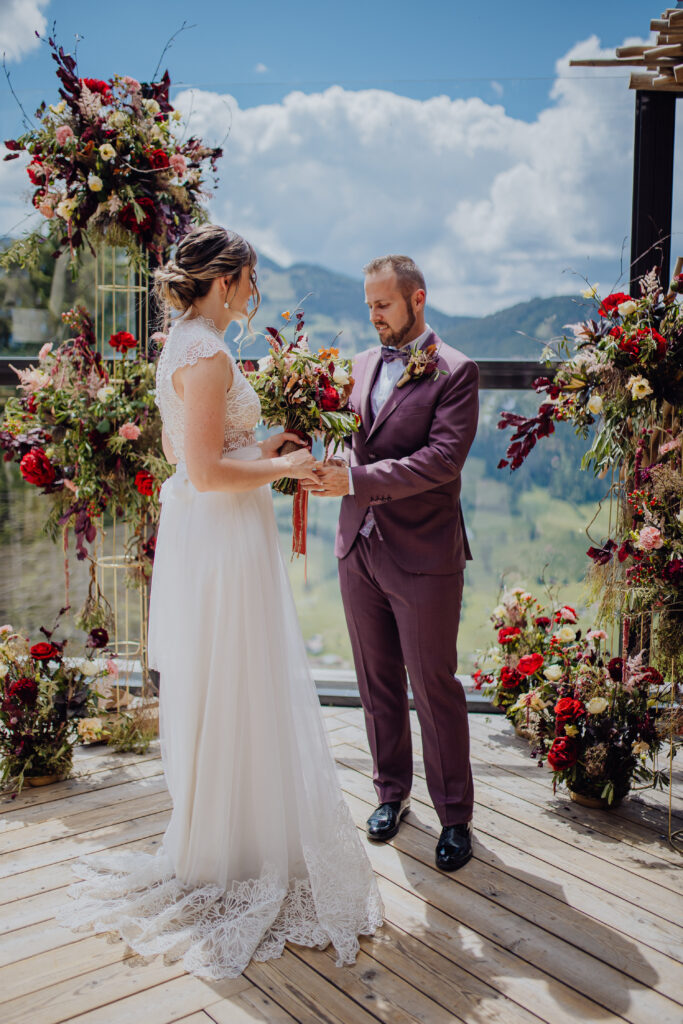Braut und Bräutigam tauschen ihr Eheversprechen unter freiem Himmel in einer atemberaubenden Hochzeitslocation in Österreich aus, umgeben von Blumenarrangements und einer atemberaubenden Bergkulisse. Hochzeitslocation Tom Almhütte in den Salzburger Bergen