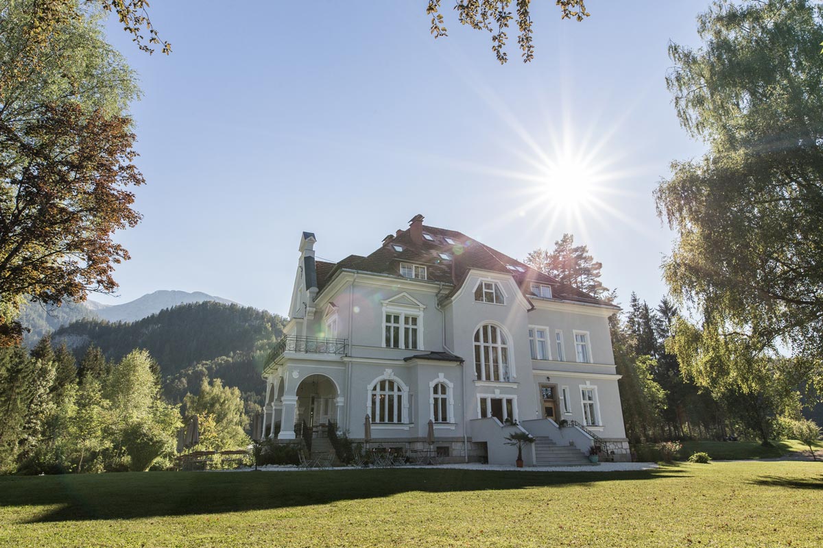 Alttext:Elegante Hochzeitslocation im Grünen mit historischer Villa, weitläufigem Garten und Bergpanorama bei Sonnenschein in Österreich. Hochzeitslocation in Österreich Villa Bergzauber