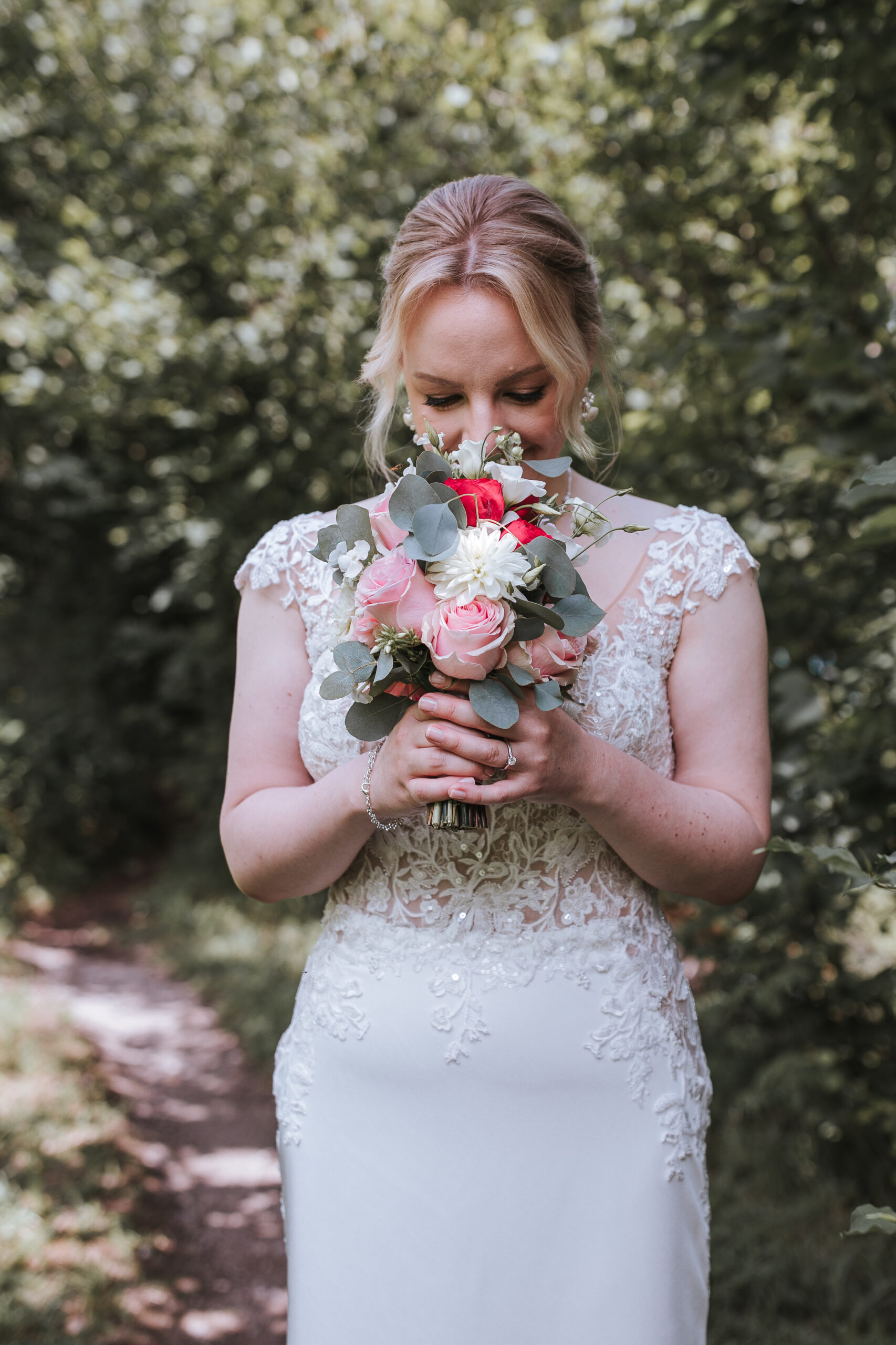 Eine Braut in einem weißen Spitzenkleid, die bei ihrer Hochzeit in Österreich im Freien einen Strauß aus rosa und weißen Blumen in den Händen hält und daran riecht.