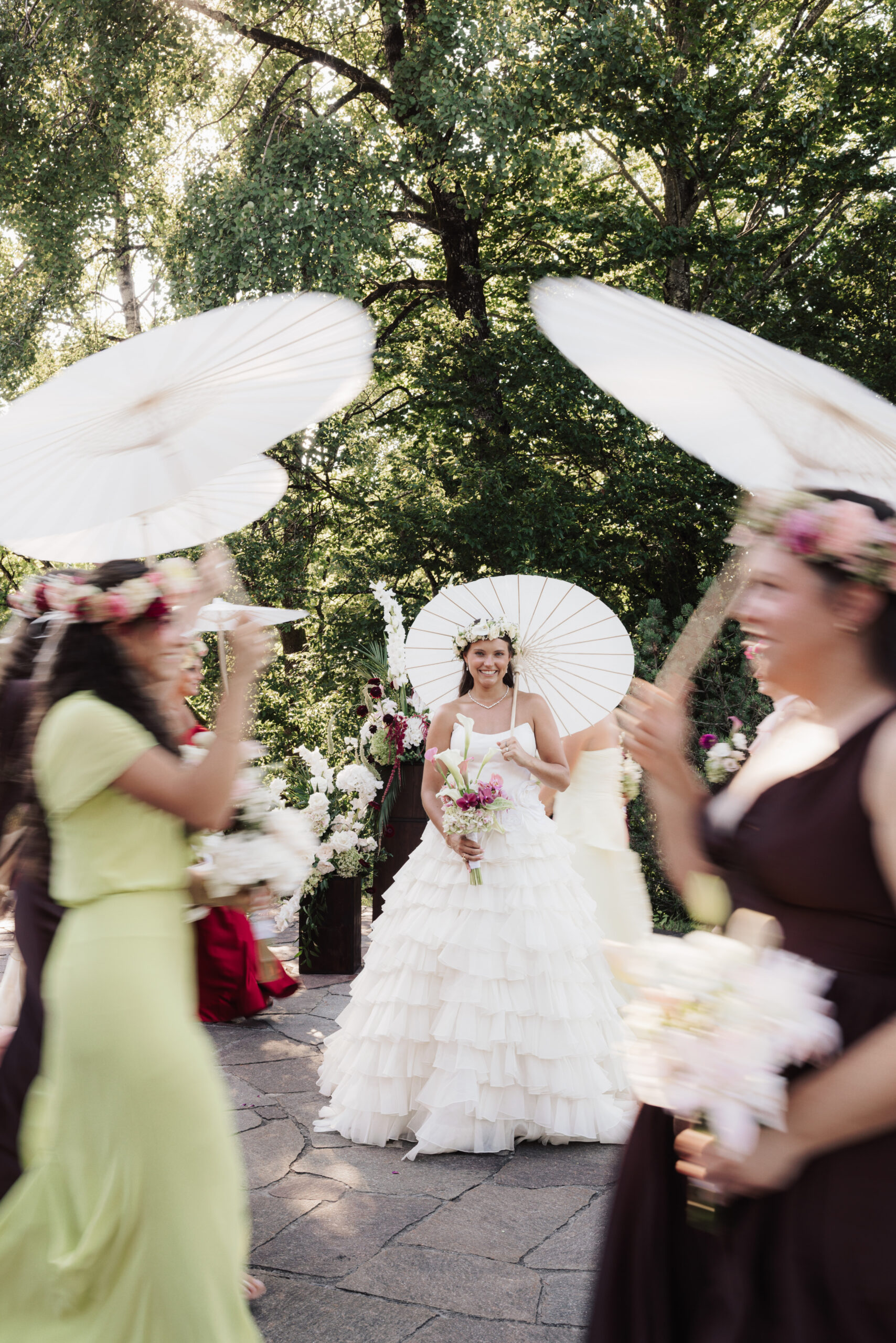 Eine Braut in einem weißen Kleid mit Sonnenschirm, umgeben von Brautjungfern, die Sonnenschirme und Blumensträuße halten – ein Bild, das die Eleganz einer Hochzeit perfekt einfängt, während jedes Detail von einem engagierten Hochzeitskoordinator sorgfältig aufeinander abgestimmt wird.