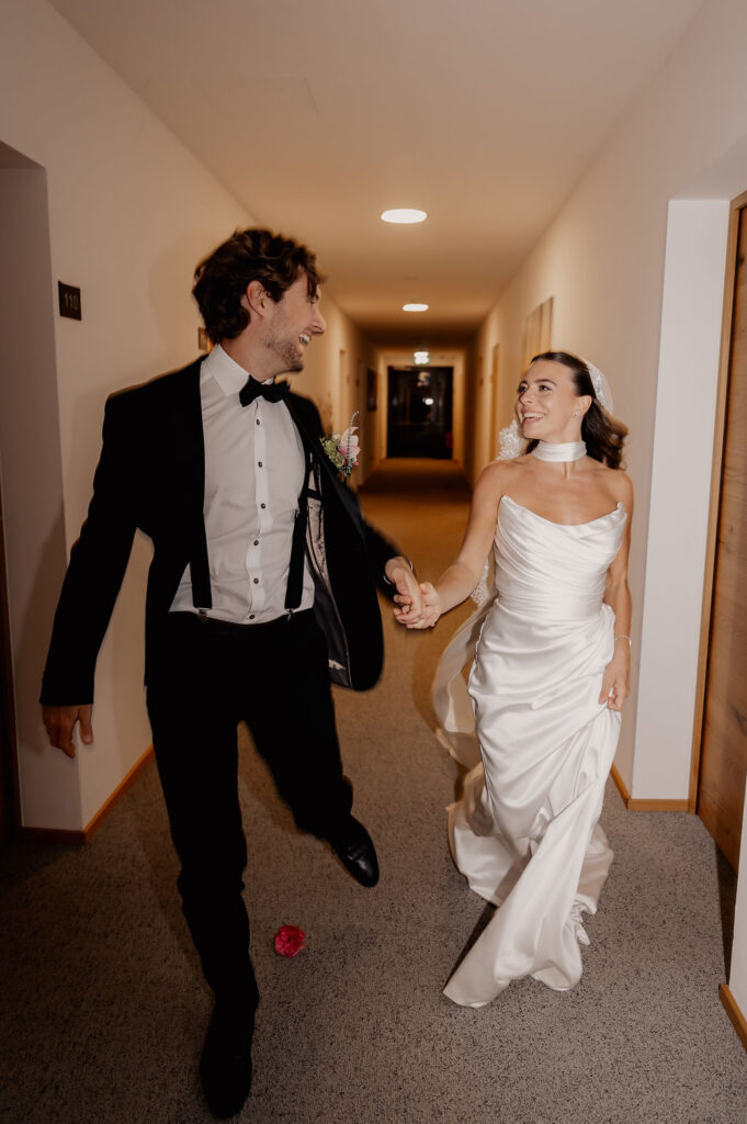 Braut und Bräutigam gehen Hand in Hand und lächelnd gemeinsam in ihrer Hochzeitskleidung einen Flur entlang und strahlen vor Freude, während sie ihre wunderschöne Hochzeit am Reiseziel feiern.