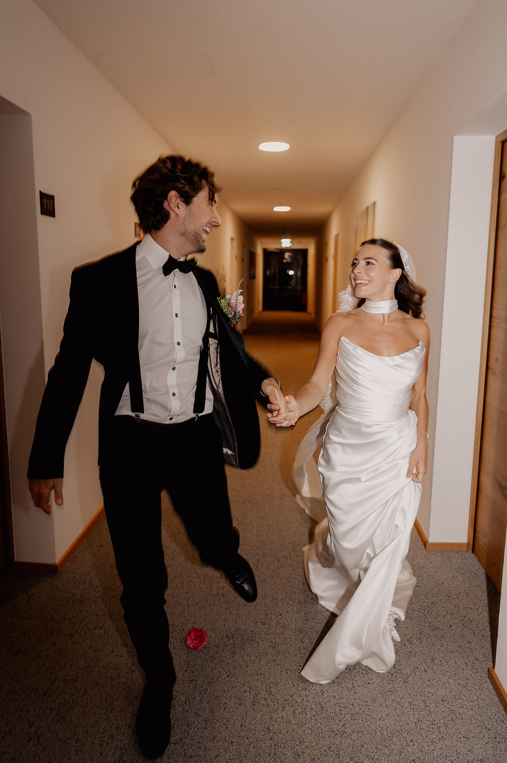 Braut und Bräutigam gehen Hand in Hand und lächelnd gemeinsam in ihrer Hochzeitskleidung einen Flur entlang und strahlen vor Freude, während sie ihre wunderschöne Hochzeit am Reiseziel feiern.