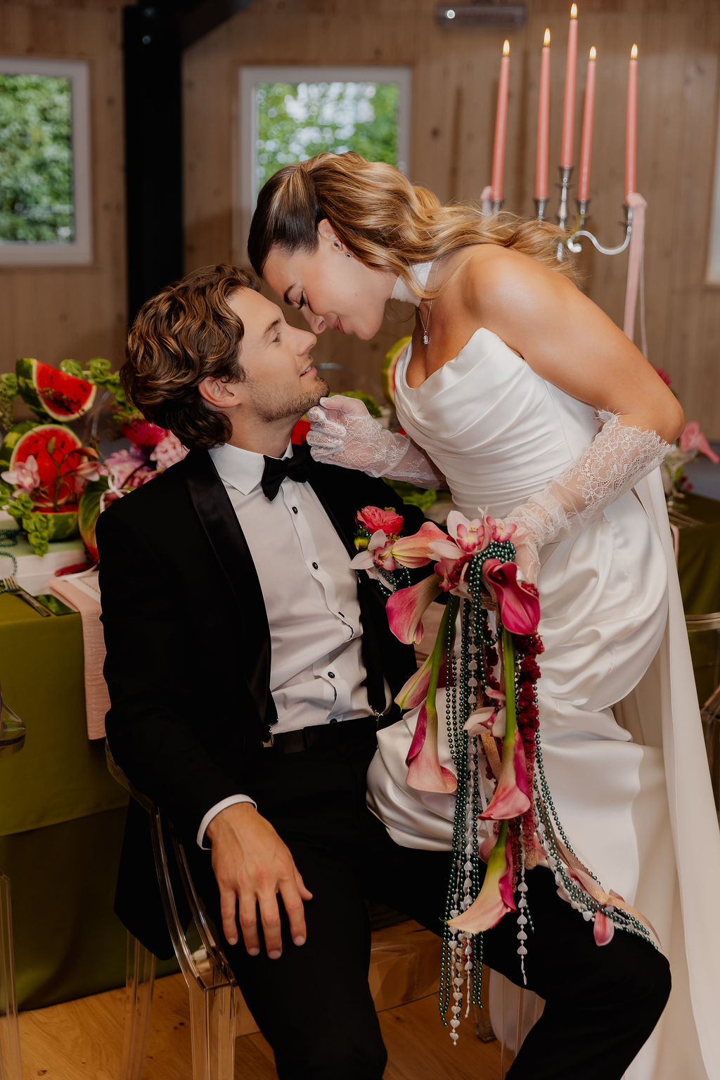 Die Braut in ihrem weißen Kleid beugt sich dem Bräutigam im Smoking nahe, den Blumenstrauß in der Hand, an einem wunderschön dekorierten Empfangstisch während ihrer Hochzeit im Ausland.
