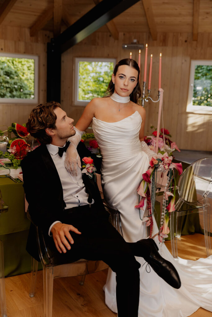 Die Braut im weißen Brautkleid und der Bräutigam im schwarzen Smoking posieren in einem eleganten, mit Blumen geschmückten Raum mit Holzwänden und -fenstern und verkörpern so den Charme einer Hochzeit im Ausland.