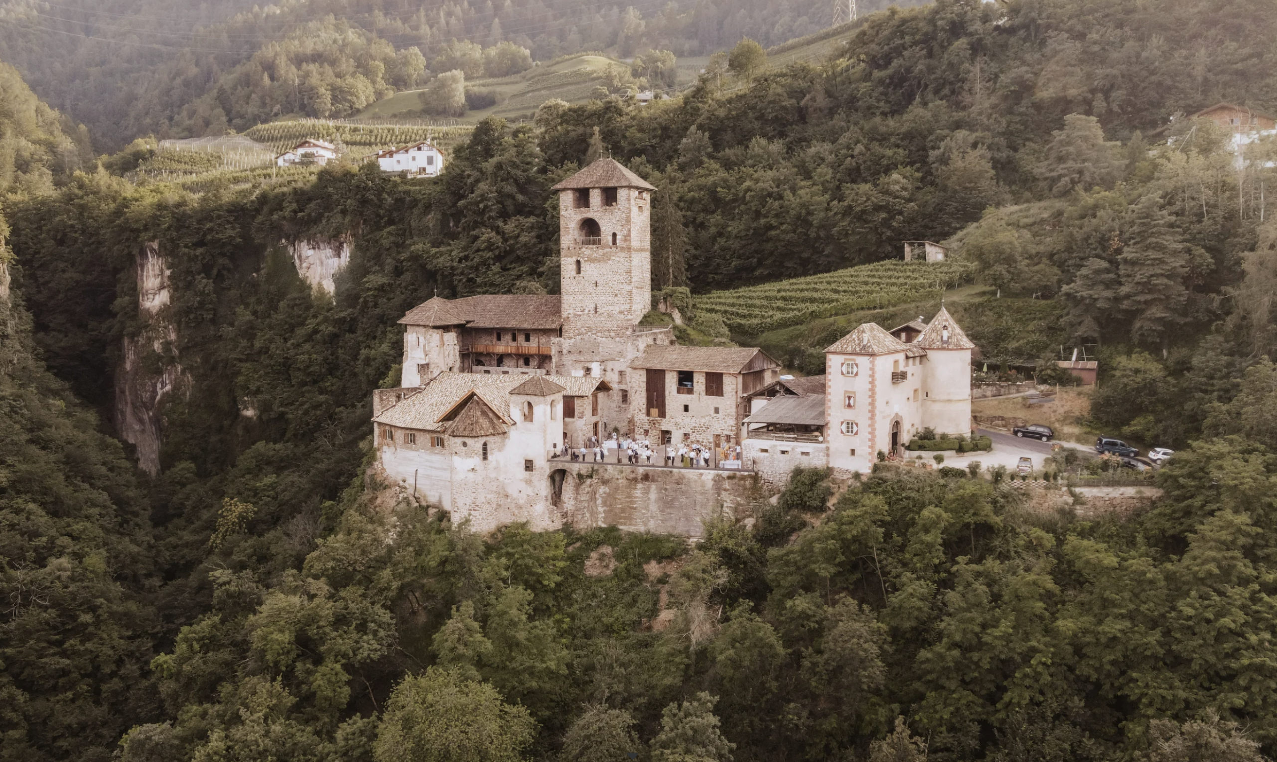 Eine mittelalterliche Steinburg mit einem hohen Turm, umgeben von Bäumen und Hügeln, aus der Vogelperspektive betrachtet – ein bezaubernder Anblick, der an die märchenhaften Hochzeitslocations in Südtirol erinnert.