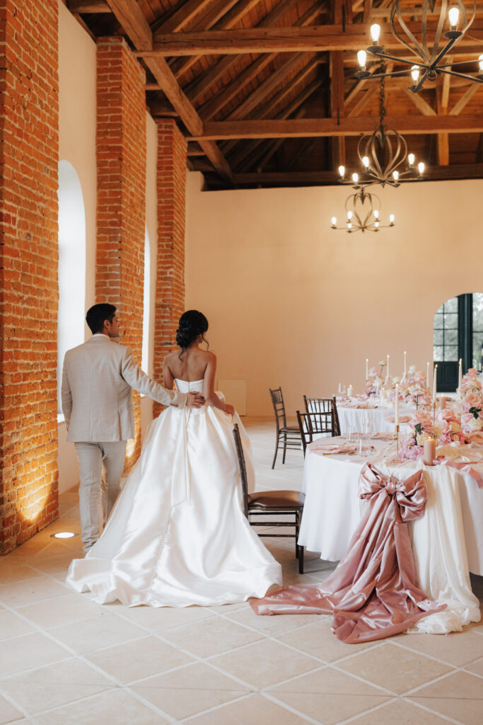Braut und Bräutigam in eleganter Kleidung schreiten auf die festlich gedeckten Tische in einer rustikalen Hochzeitslocation mit Backsteinwänden zu – einer der schönsten Orte für eine unvergessliche Hochzeit und eine beliebte Hochzeitslocation in Oberösterreich.