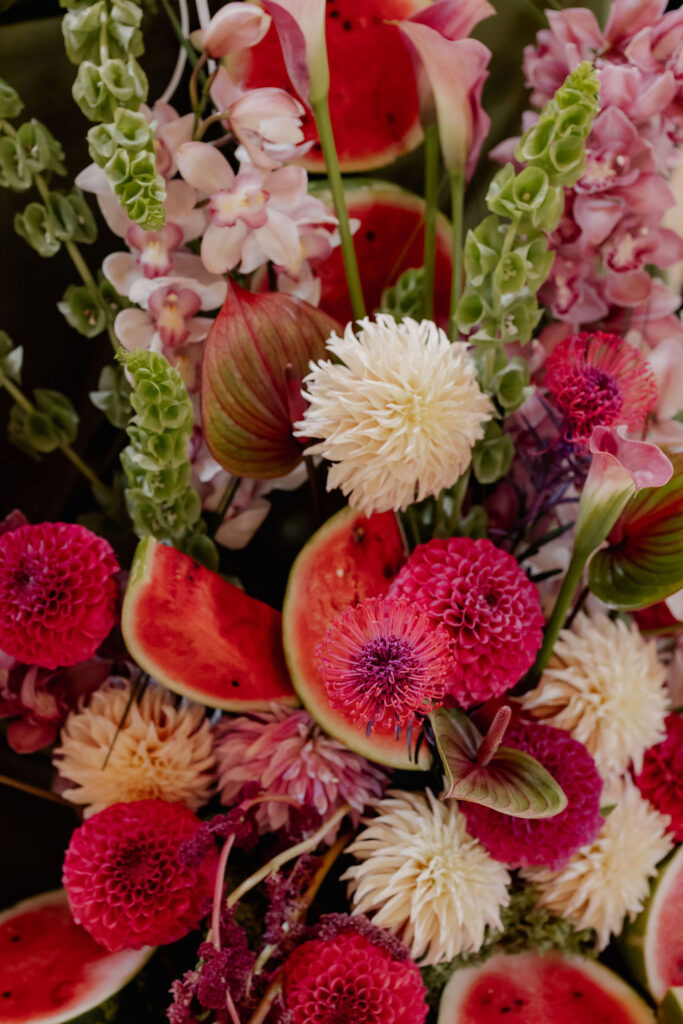Farbenfrohes Blumenarrangement mit roten Dahlien und weißen Blüten, akzentuiert durch Wassermelonenscheiben – die perfekte Inspiration für die Tischdekoration an Hochzeitslocations in Salzburg Stadt.